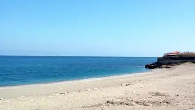 a beach with blue water and a house in the background at Casa Dadà, romantic house in historic centre in Palermo