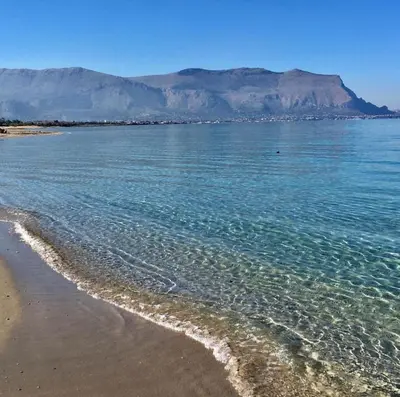a beach with blue water and a mountain in the background at Goccia del mare in Isola delle Femmine