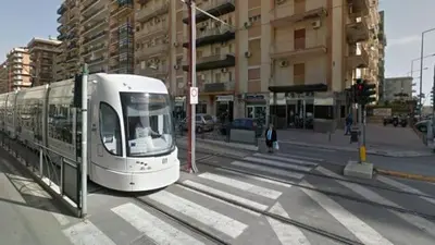 a white train on a city street with buildings at Maya's Apartment close to Ballarò Market and Central station in Palermo