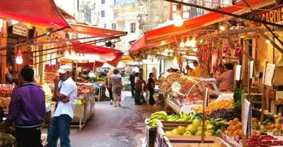 a group of people walking around a market with fruits and vegetables at Maya's Apartment close to Ballarò Market and Central station in Palermo