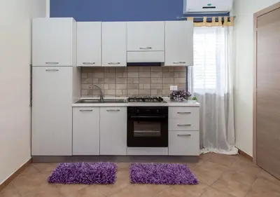 a kitchen with white cabinets and purple mats on the floor at Casa vacanze Biondo in Trappeto