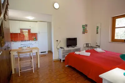 a bedroom with a red bed and a kitchen at Casale la Macina Residence Scopello in Scopello
