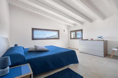 a white bedroom with a blue bed and a table at Villa vista mare con piscina a Sarmuci in Castellammare del Golfo