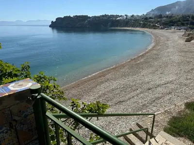 a beach with a green railing and the water at Terrazza sul mare Scopello in Scopello