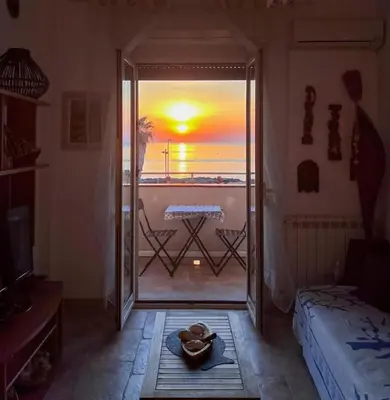 a room with a door open to a balcony with a sunset at Isola delle Femmine Holiday in Isola delle Femmine