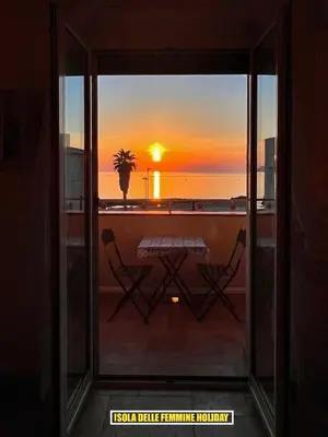 a view of a sunset from a window with a table and chairs at Isola delle Femmine Holiday in Isola delle Femmine