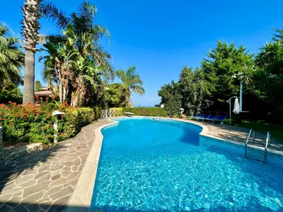 a swimming pool with blue water and palm trees at Villa Talìa in Carini