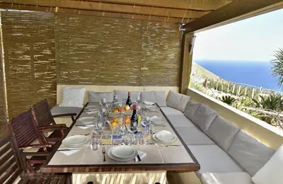 a table with plates and wine bottles on a balcony at Villa Fenice in Scopello
