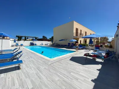 a swimming pool with chairs and umbrellas next to a building at Coral sea B2 in San Vito lo Capo