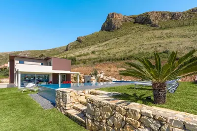 a villa with a palm tree and a stone wall at La Dolce Vita in Castellammare del Golfo