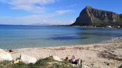 a person laying on a beach with a mountain in the background at APPARTAMENTO A SAN VITO LO CAPO STANZA CON BAGNO in San Vito lo Capo