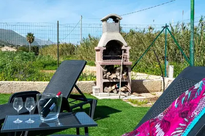 a outdoor oven with two chairs and a table with wine glasses at Federica's House - Sporting Village in Scopello