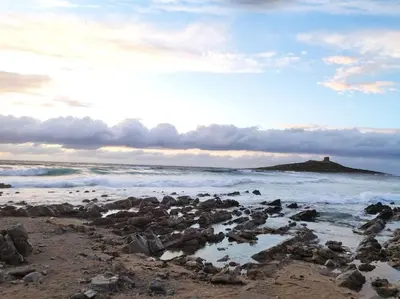 a beach with rocks and a lighthouse in the ocean at CASA 3T a Isola a 15 min dal centro di Palermo in Isola delle Femmine