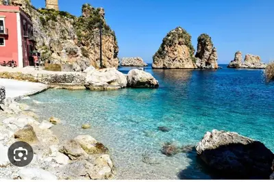 a body of water with rocks and a red building at AFFITTACAMERE LE SIGNORINE in Castellammare del Golfo