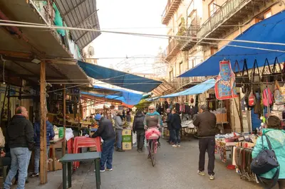 a group of people walking through an outdoor market at La Casa del Mercado in Palermo