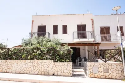 a white building with a stone wall in front of it at Casa Orchidea Nera in San Vito lo Capo