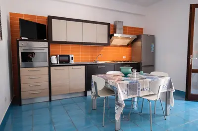 a kitchen with a table with chairs and an orange tile wall at Casa Orchidea Nera in San Vito lo Capo
