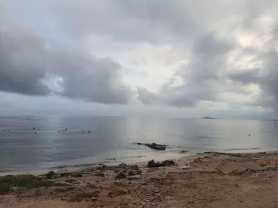 a beach with people in the water on a cloudy day at Casa Poseidonia - intero alloggio in riva al mare in Carini